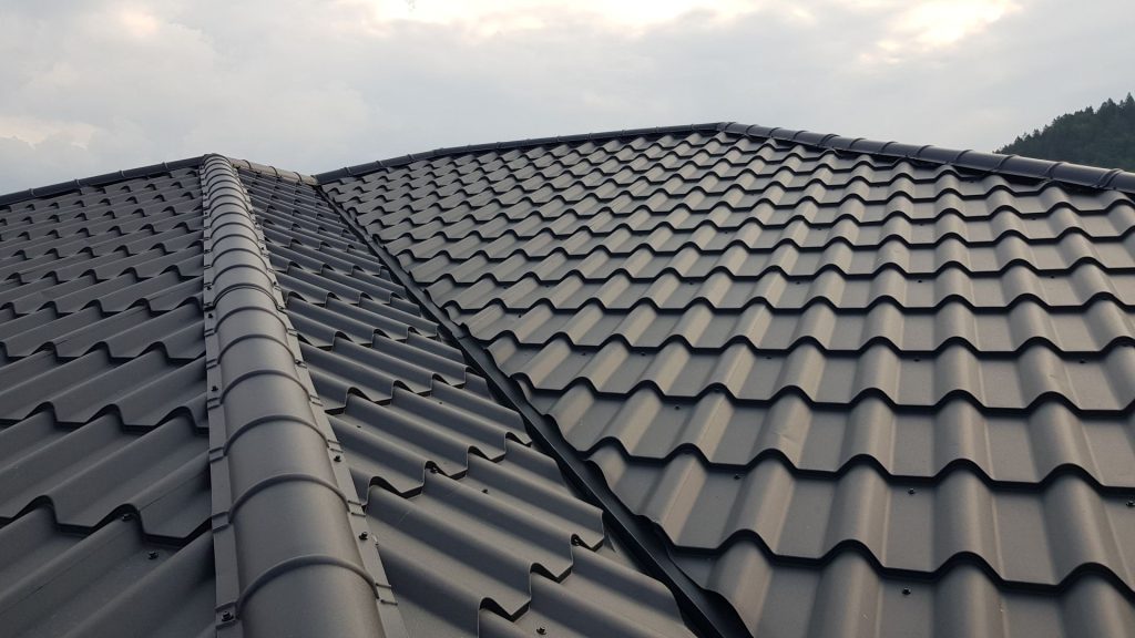 Detail tmavosivej plechovej strechy so škridlovým vzorom pod zamračenou oblohou. Vlnitý vzor vytvára jednotný a elegantný vzhľad a vyjadruje odolnosť.