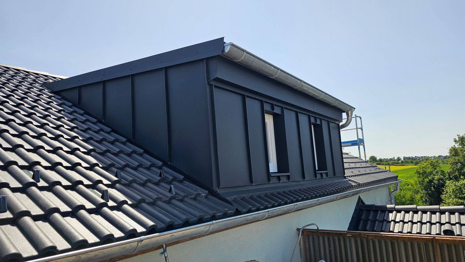 Moderná strecha domu s tmavosivými škridlami a elegantným vikierom pod jasnou oblohou. Scéna vyjadruje čistú a súčasnú atmosféru.